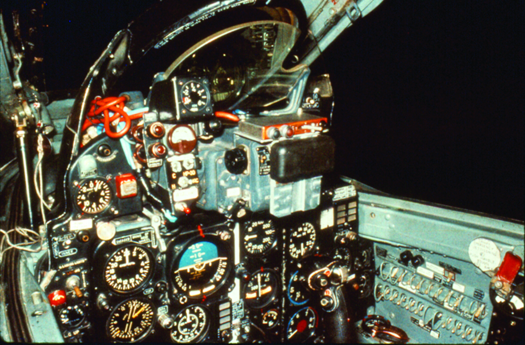 A close-up color photograph of a MiG-21 cockpit, showing a complex array of analog gauges, dials, switches, and controls on the instrument panel.